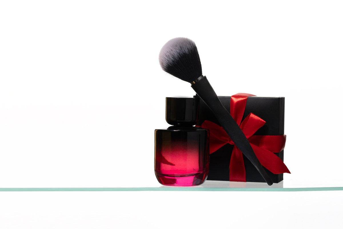 A make-up brush, a red perfume bottle and a black gift box tied with a red satin bow
