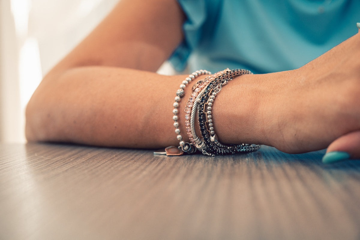 A stack of silver and beaded bracelets on a woman's wrist resting on a table
