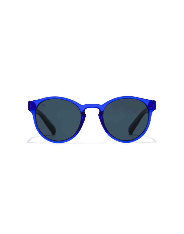 Hawkers round kids sunglasses, transparent blue plastic frame, keyhole bridge, dark round lenses