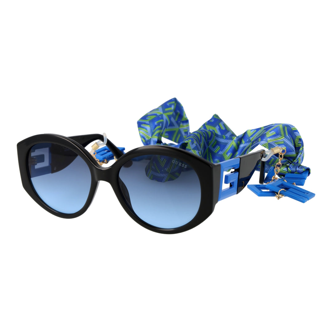 Black cat-eye sunglasses with gradient blue lenses, blue-green patterned scarf and gold chain charms