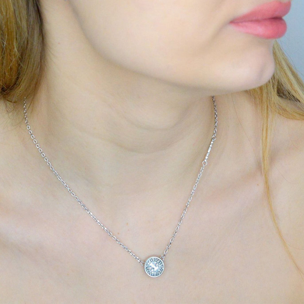 Silver pendant necklace on delicate chain featuring clear round stone and small triangular charm